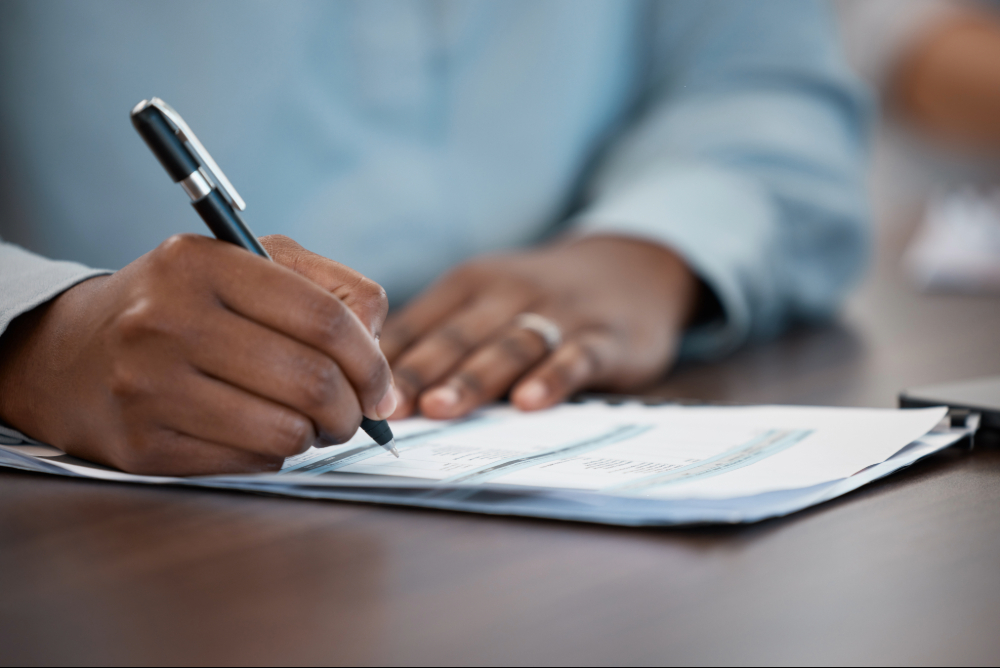 Person signs a form that's laying on a table.